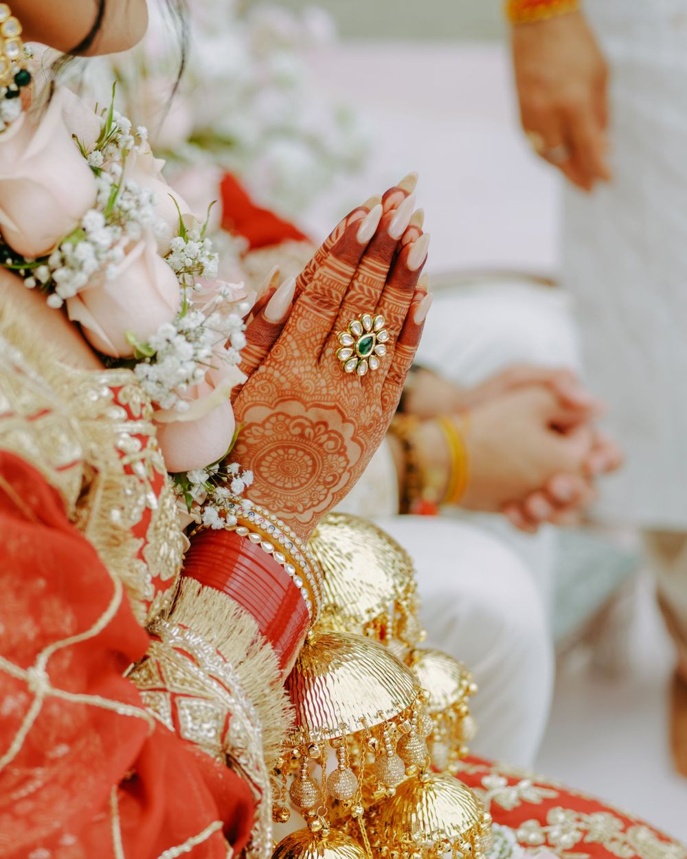 Intricate henna designs adorn hands adorned with gold bangles and baby's breath flowers at an Indian wedding ceremony.