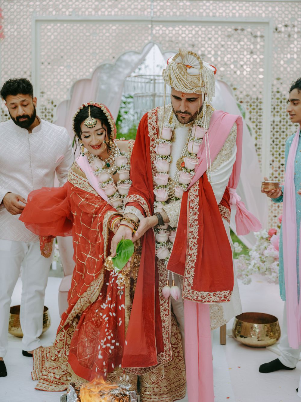 Traditional Indian wedding ceremony with couple in red and pink attire performing rituals under decorated mandap.