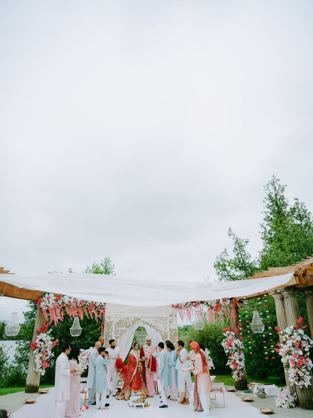 Outdoor wedding ceremony setup with white canopy decorated with pink floral arrangements and hanging glass orbs.