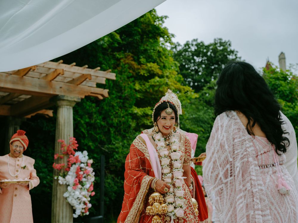 Traditional South Asian wedding ceremony under a wooden mandap decorated with pink and white flowers in an outdoor garden setting.