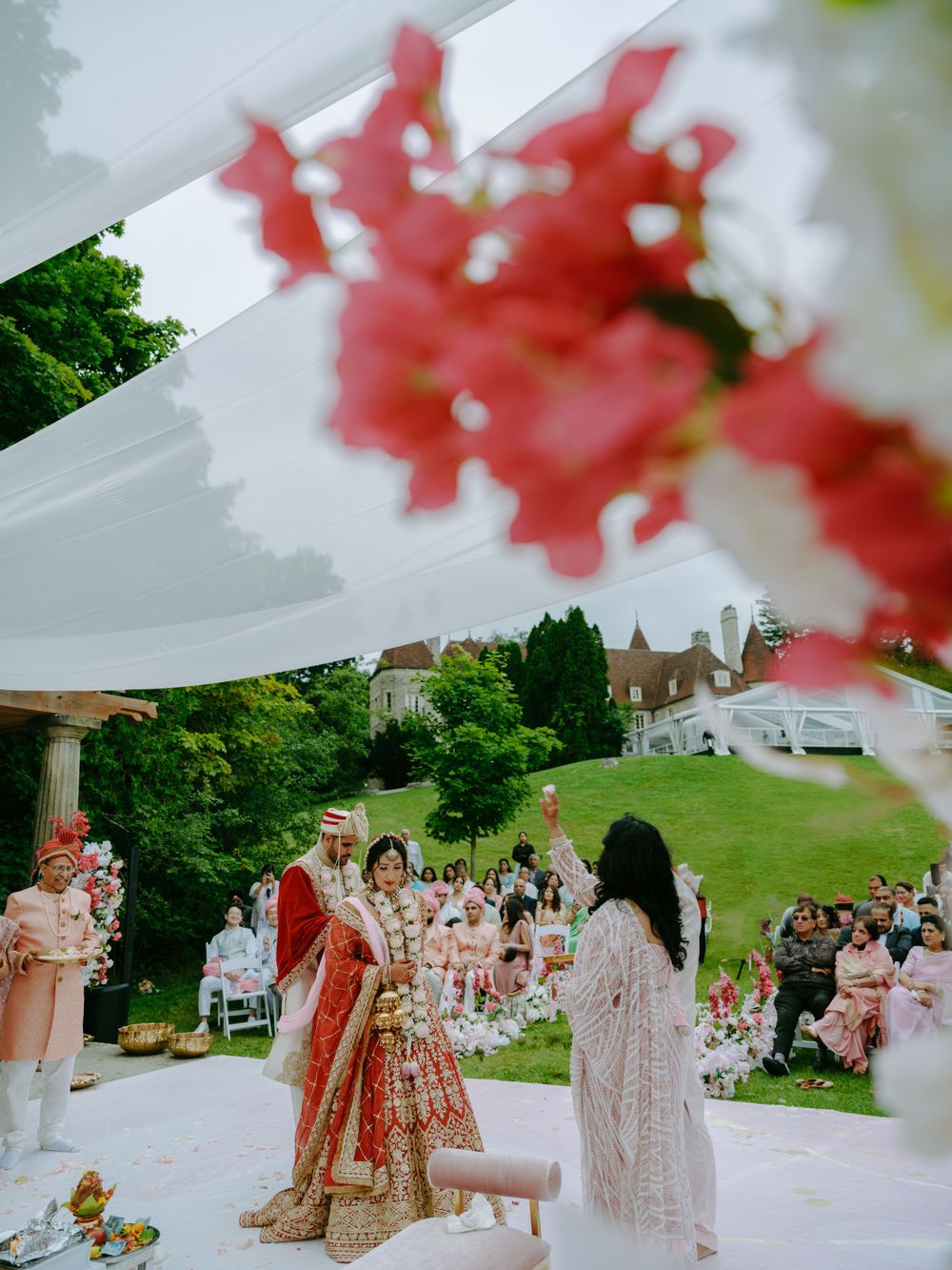 Traditional Indian wedding ceremony taking place outdoors under a white canopy with red floral decorations.