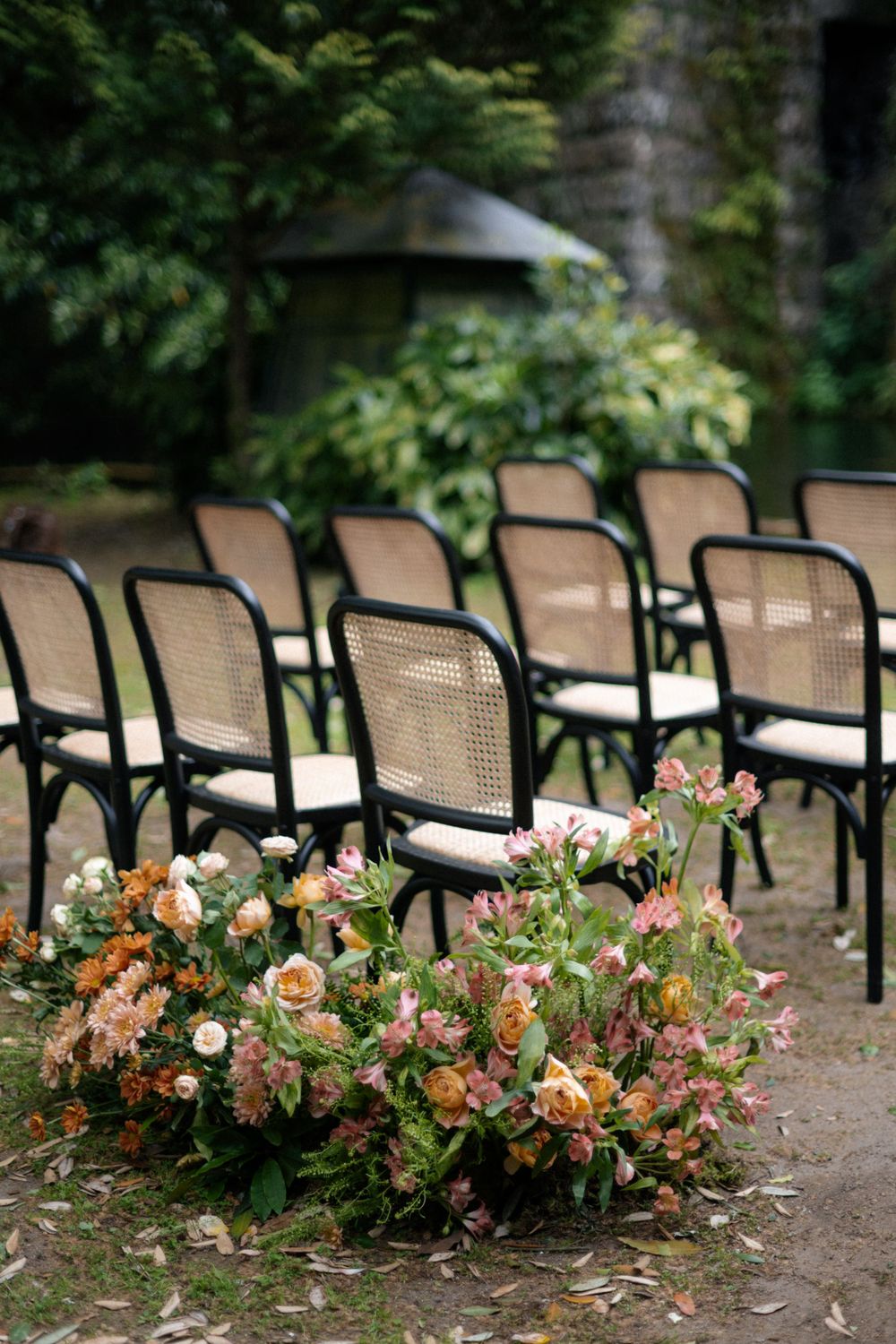 Elegant wedding ceremony setup with cane back chairs and lush floral arrangements in peach and pink tones.
