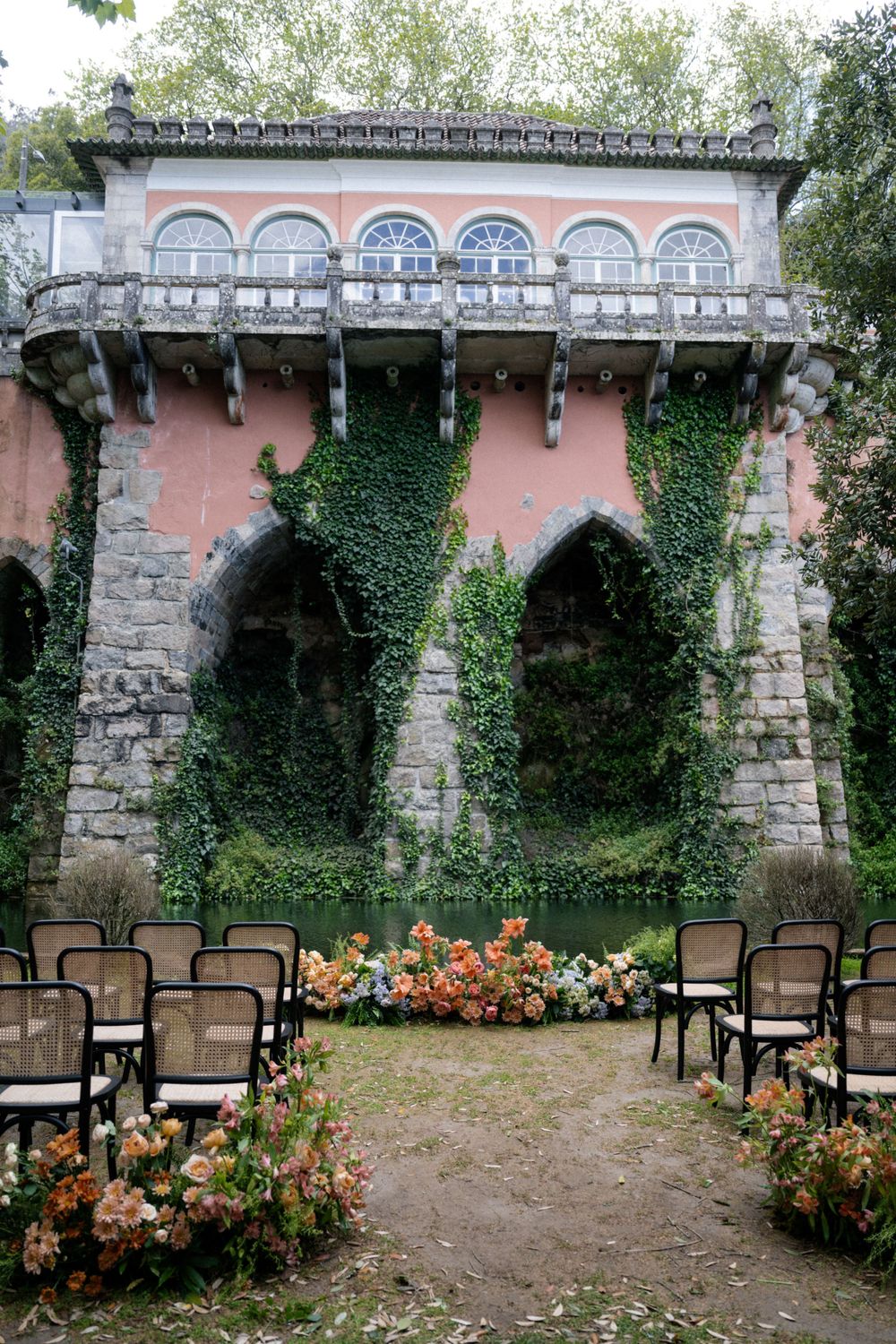 Pink stone wedding venue with arched architecture and ivy, chairs set up for outdoor ceremony.