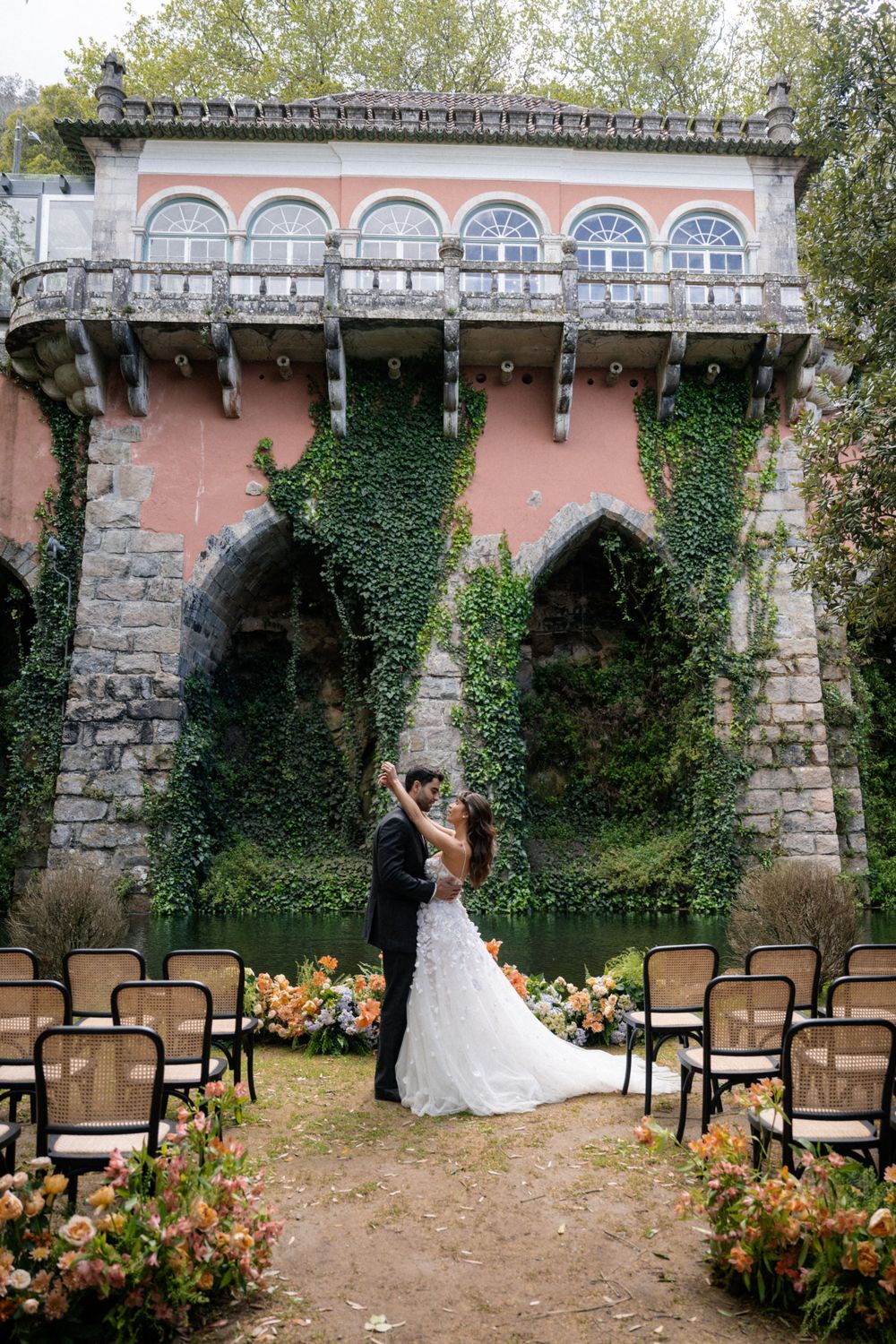 Outdoor wedding ceremony space with stone archways, pink walls, and floral decorations.