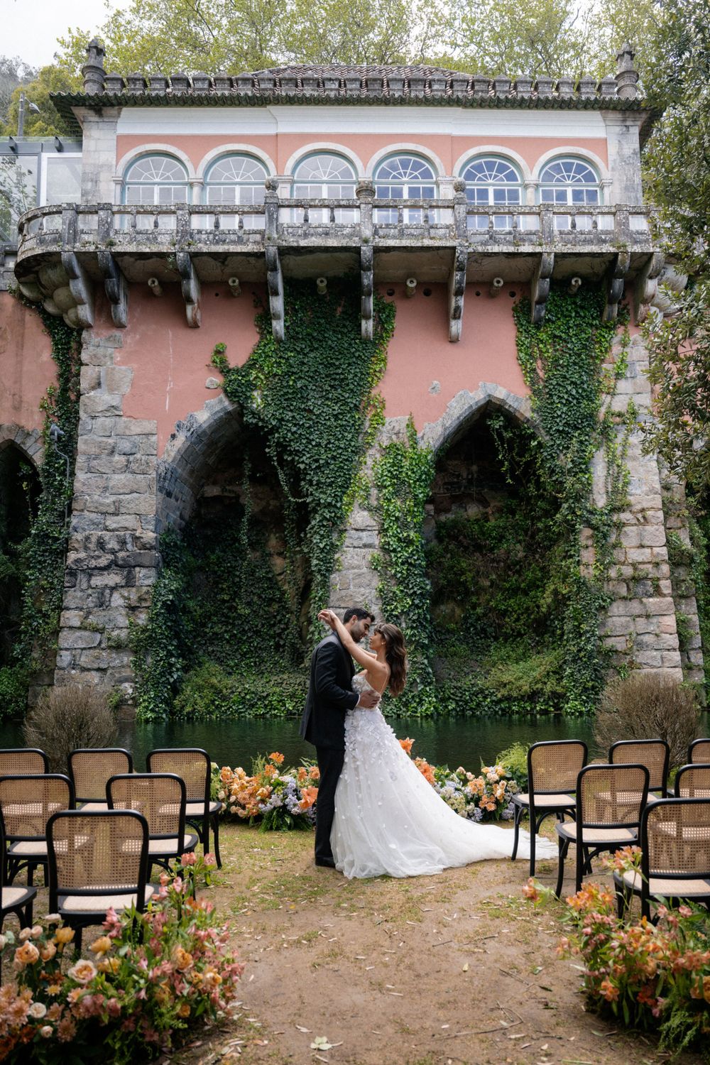 Classic outdoor wedding setup with stone architecture, pink walls, and peach floral arrangements.