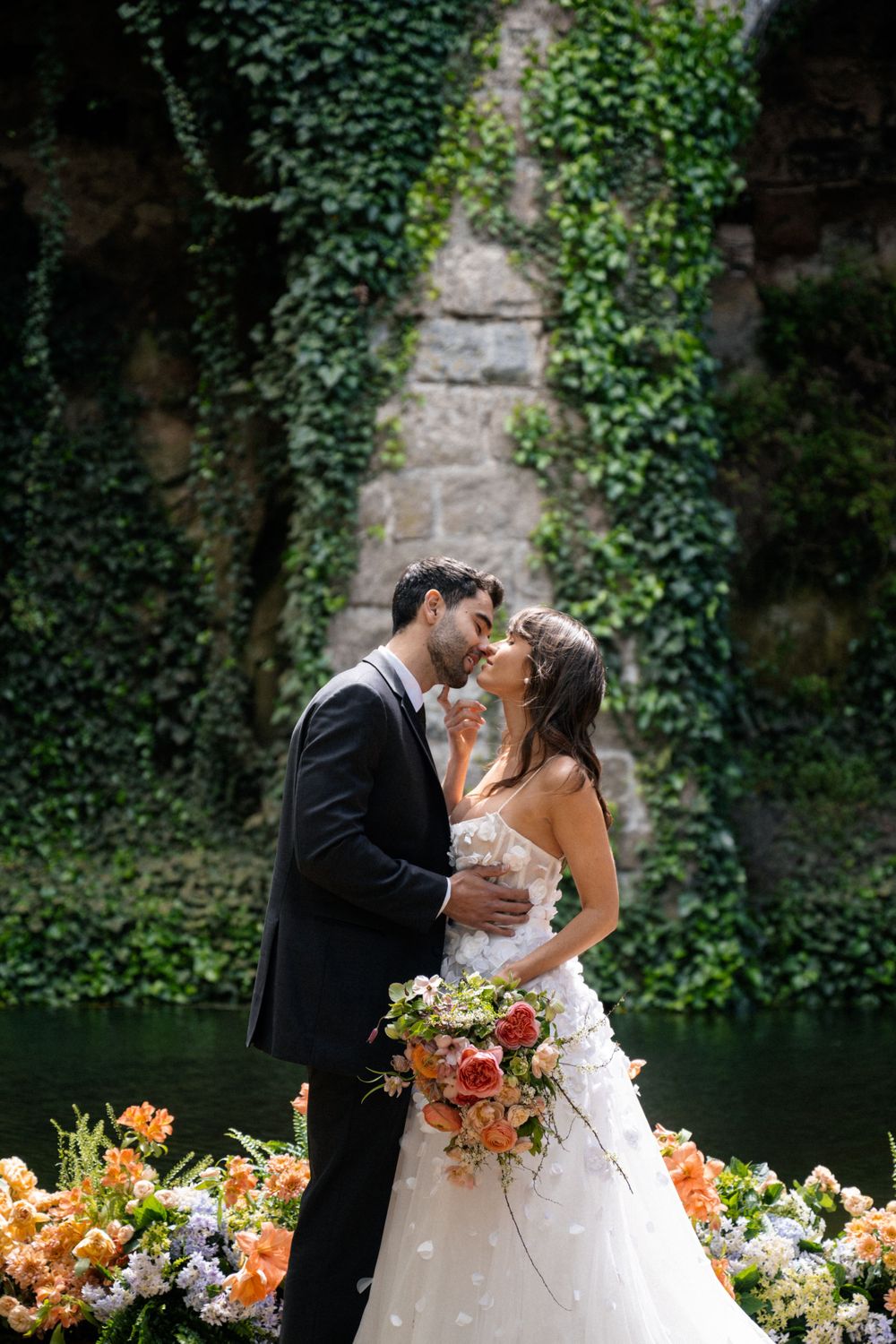 Intimate wedding moment captured by stone wall with lush floral arrangements.