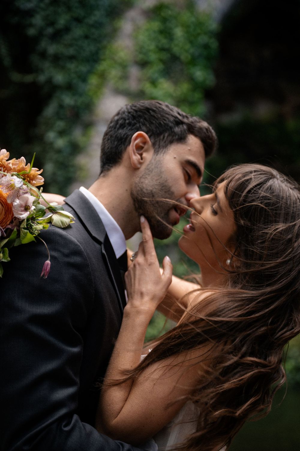 A romantic embrace captured during a wedding photoshoot against an ivy-covered stone wall.
