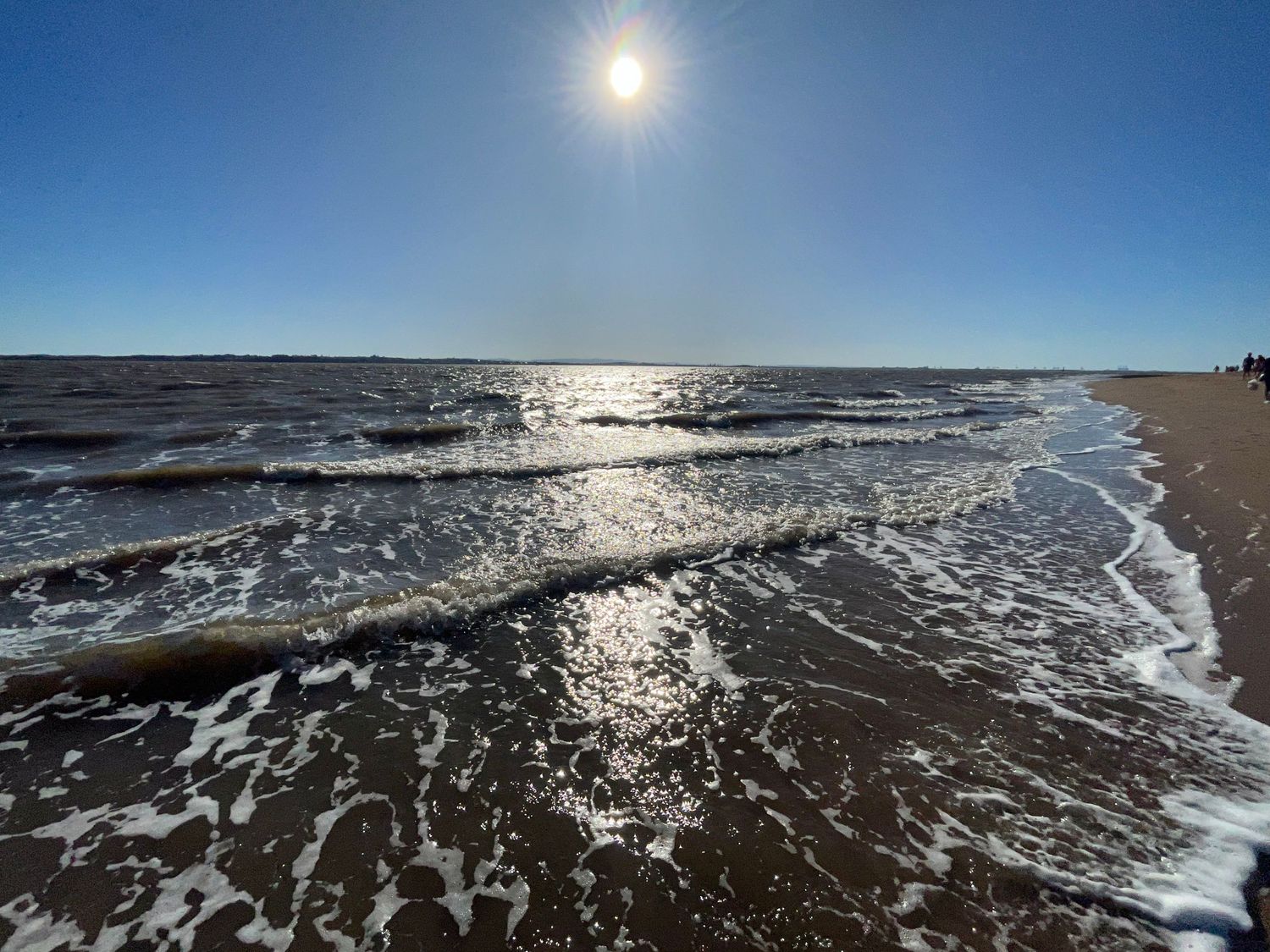Panoramic view of a sunlit ocean coastline with waves crashing on the shore.