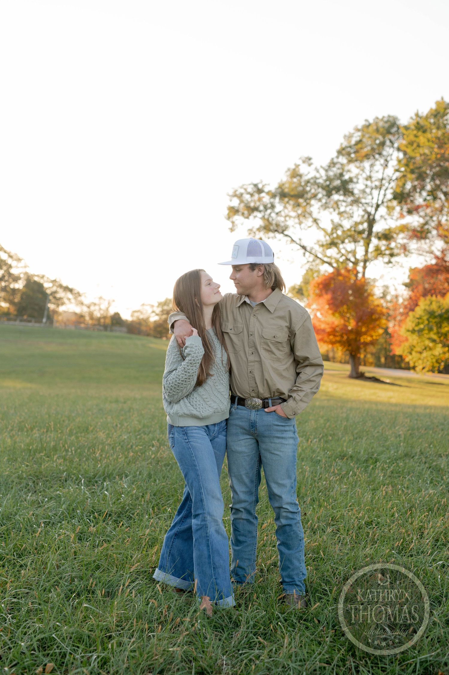 A tender moment between a couple standing in a sunlit field during golden hour.