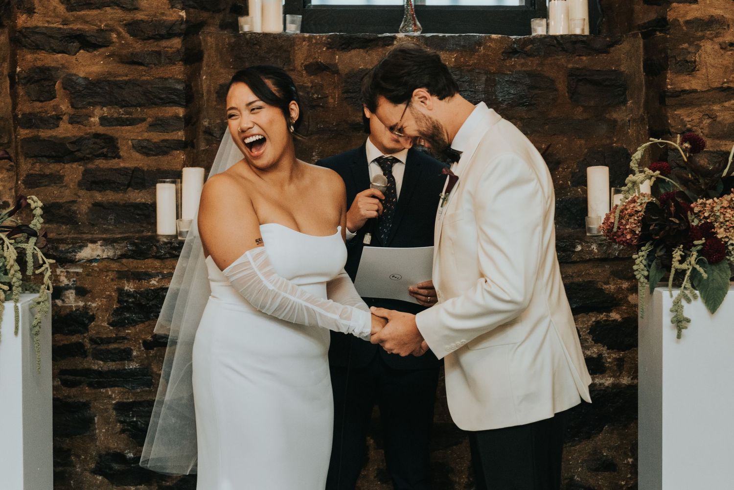 A joyful wedding moment shows emotional reactions during the ceremony in front of a rustic brick wall.