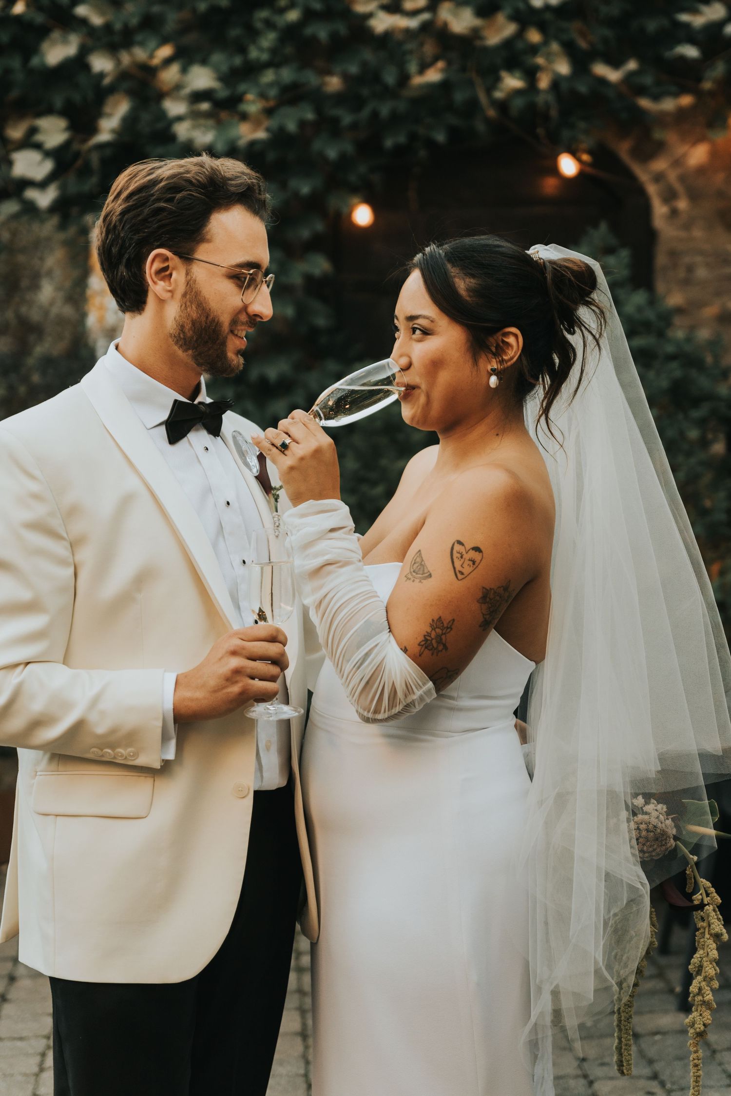 A romantic moment between newlyweds at an outdoor wedding with string lights and greenery in the background.