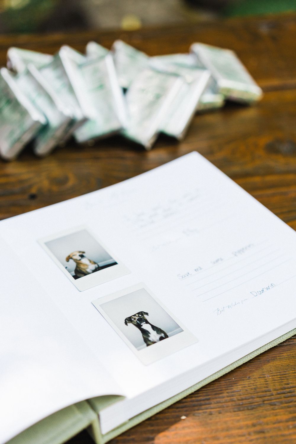 Photo album open on wooden table displaying polaroid images with white photograph storage in background.
