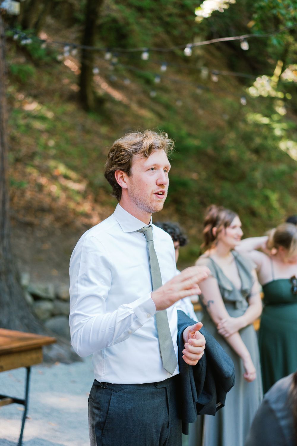 Wedding guest in white shirt and tie speaking at an outdoor forest venue.