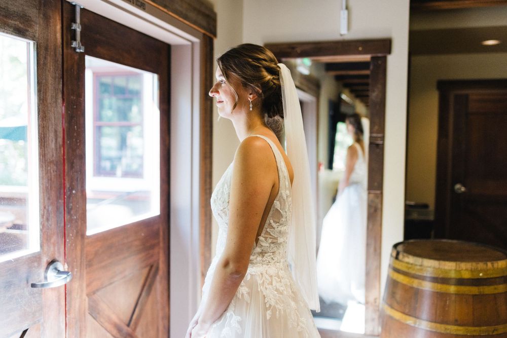 A bride in a delicate lace wedding gown stands beside a rustic wooden door in anticipation of her ceremony.