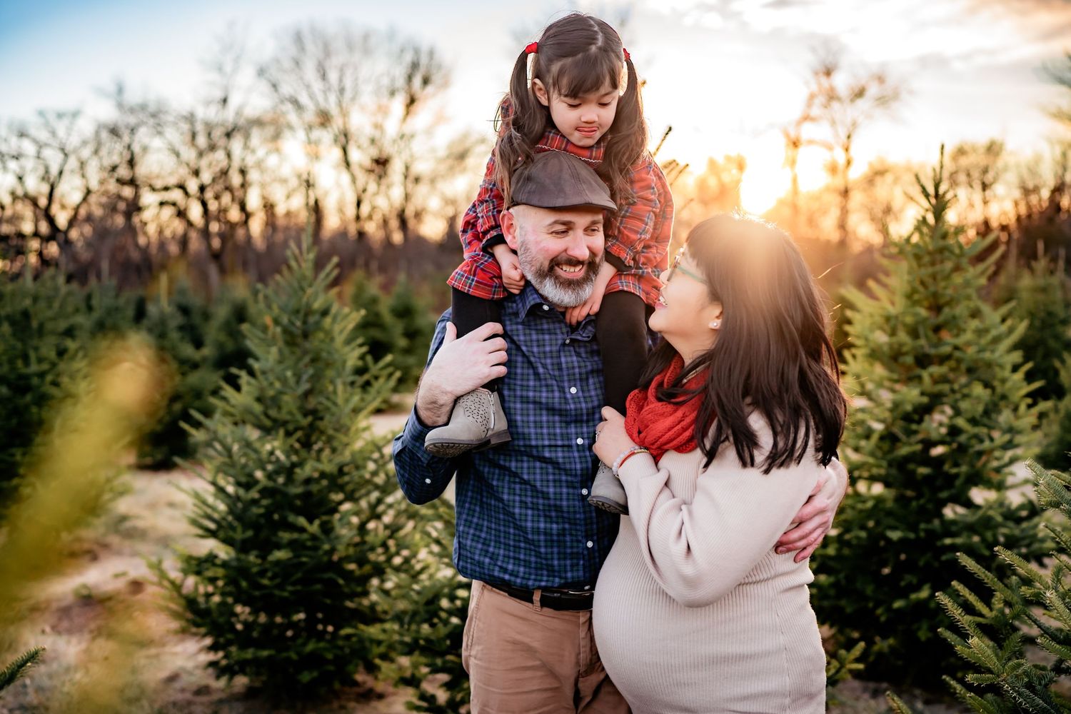 A family shares a joyful moment together among evergreen trees at a Christmas tree farm during golden sunset.