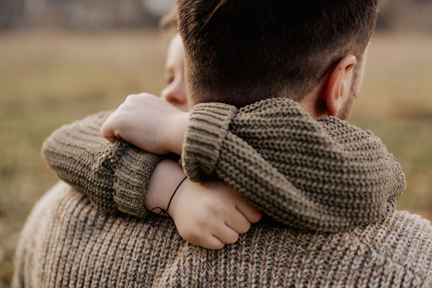 An intimate embrace shows two people hugging while wearing cozy knit sweaters in warm autumn lighting.