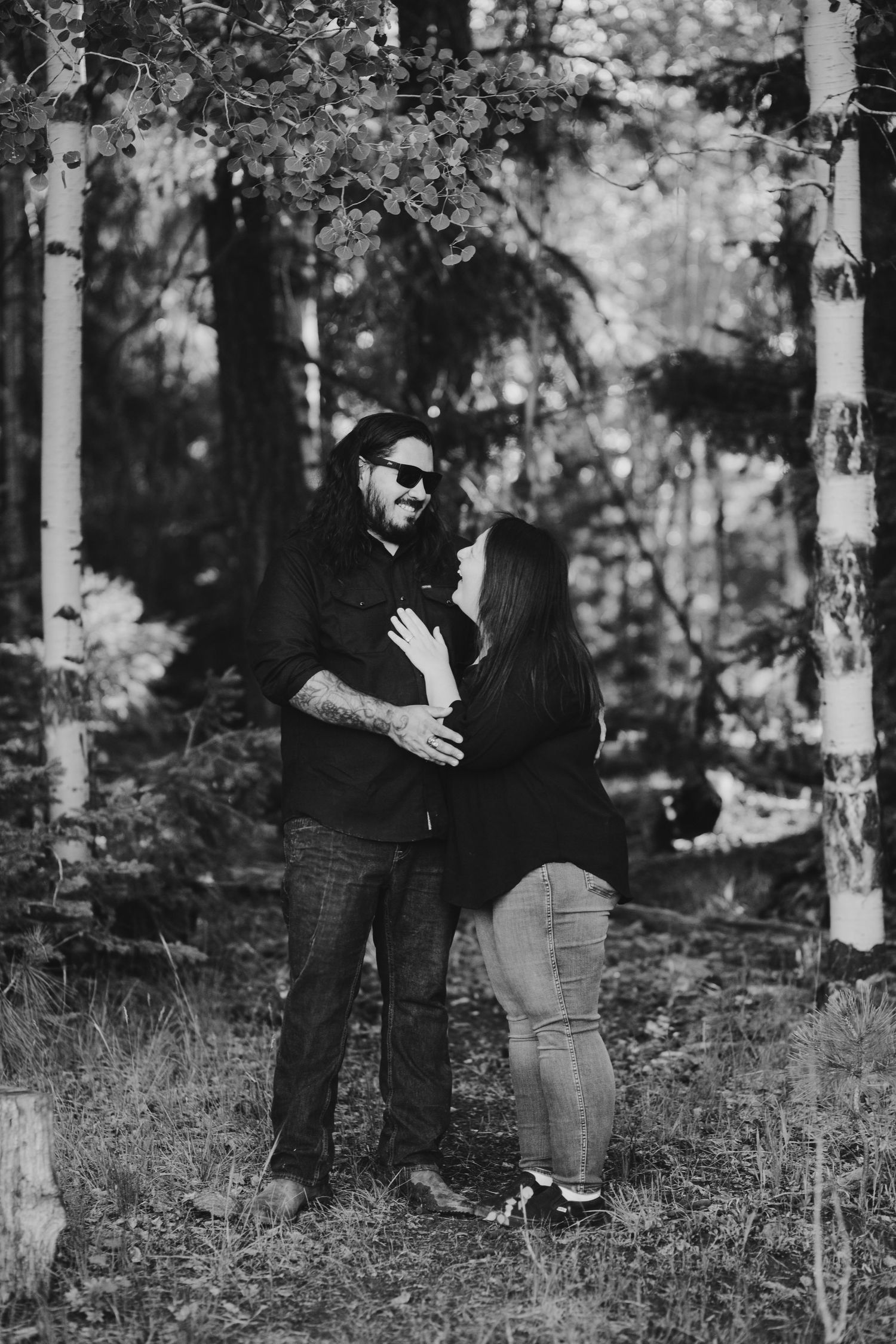 A couple embraces in a romantic forest photoshoot among tall trees.