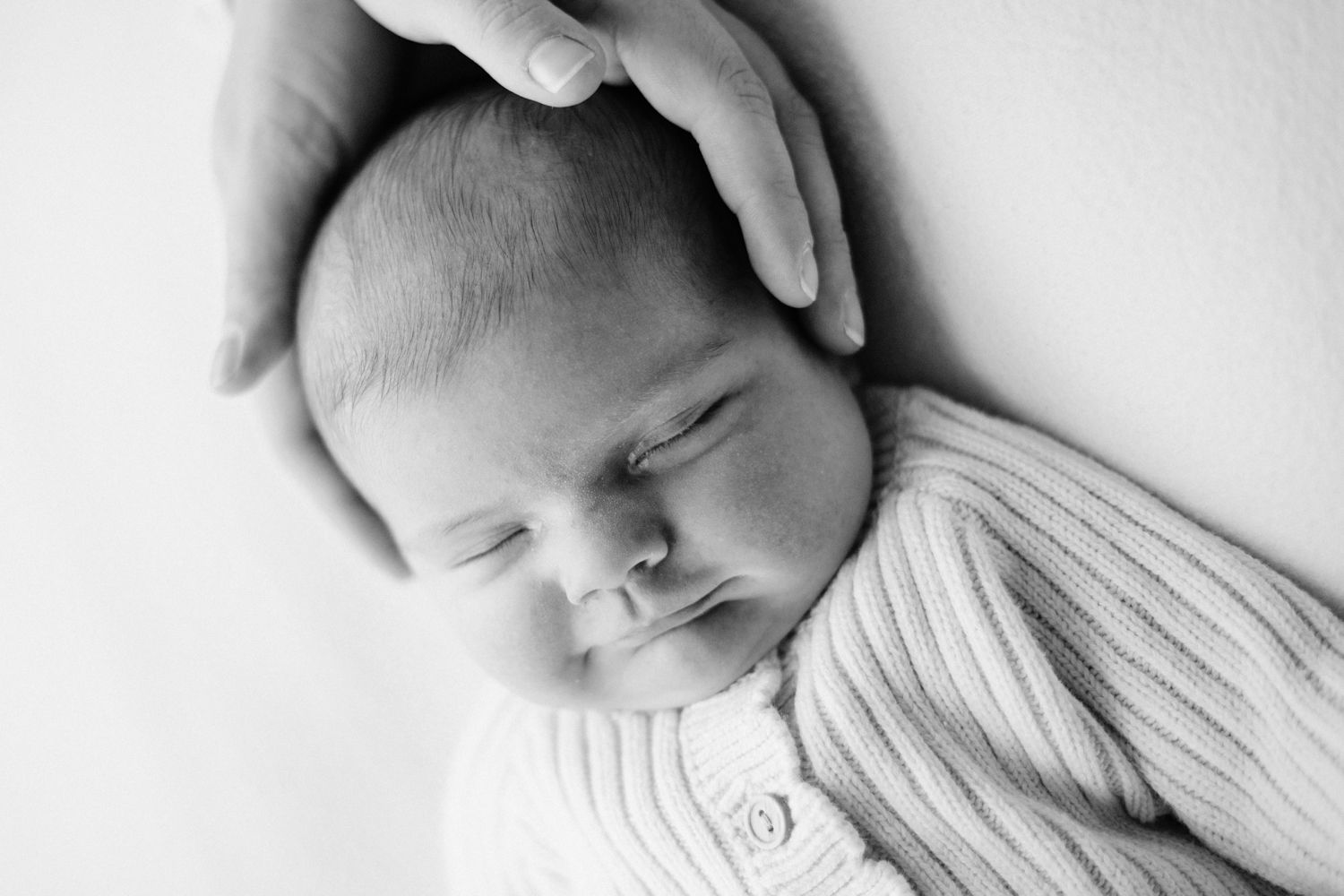 A peaceful sleeping newborn baby wearing a white cardigan sweater in a black and white portrait.