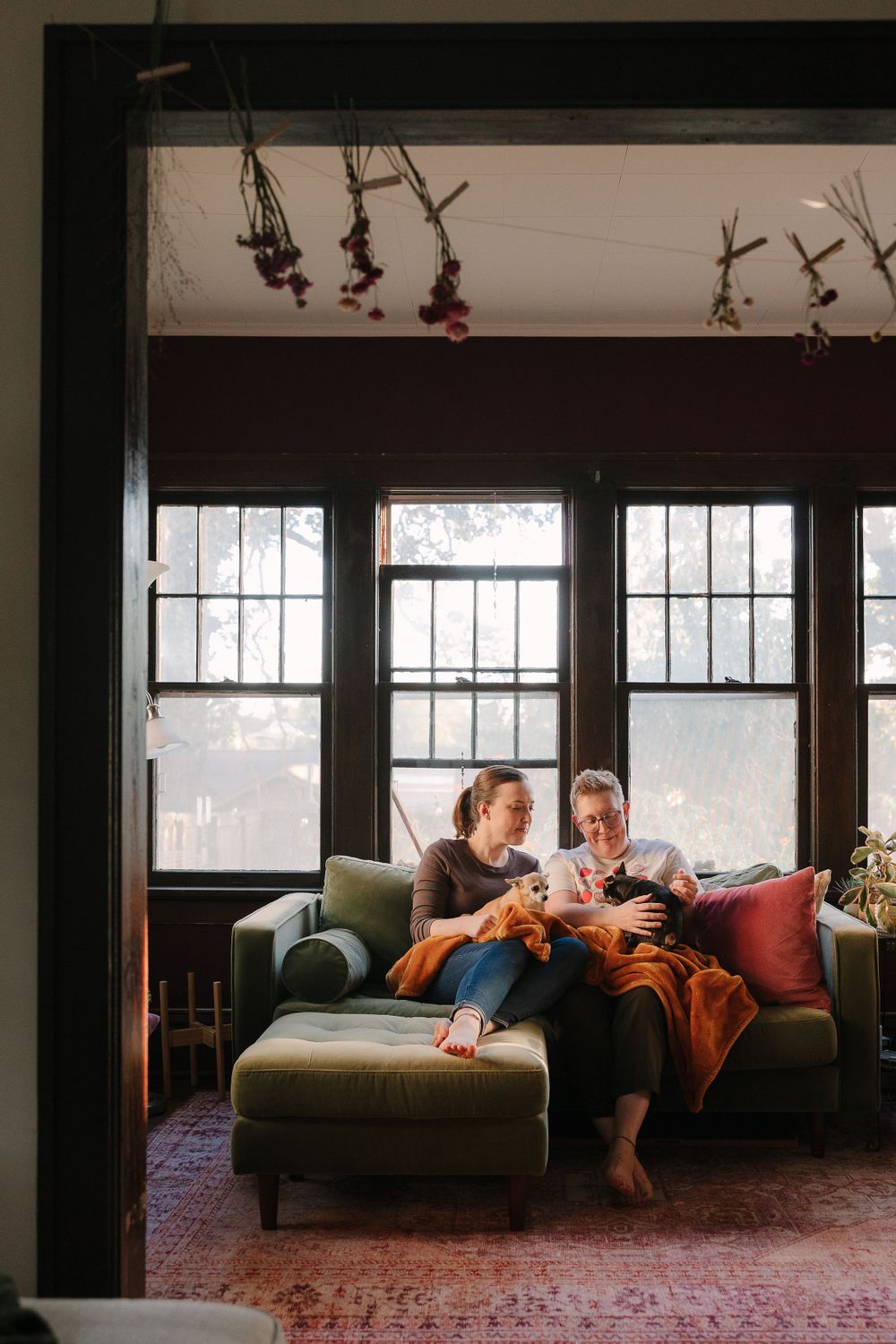 Two women snuggle their small dogs on a couch in their home.