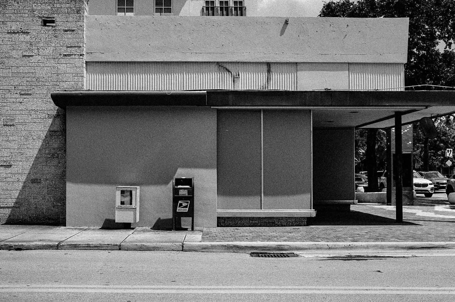 Exterior view of a small commercial storefront with a newspaper dispenser box beside a covered entrance area.
