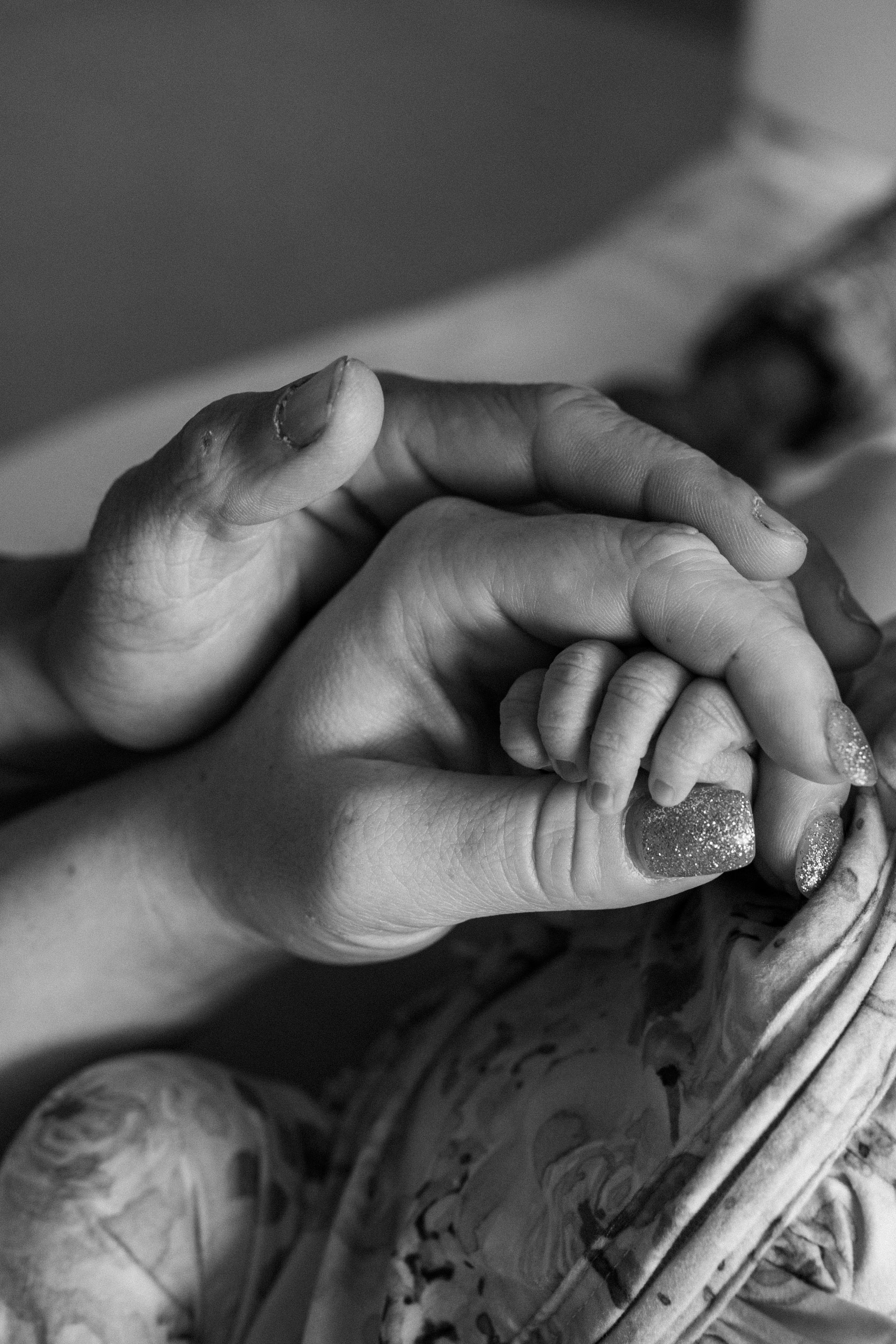 Black and white close-up photograph showing adult and baby hands tenderly clasped together in an intimate moment.