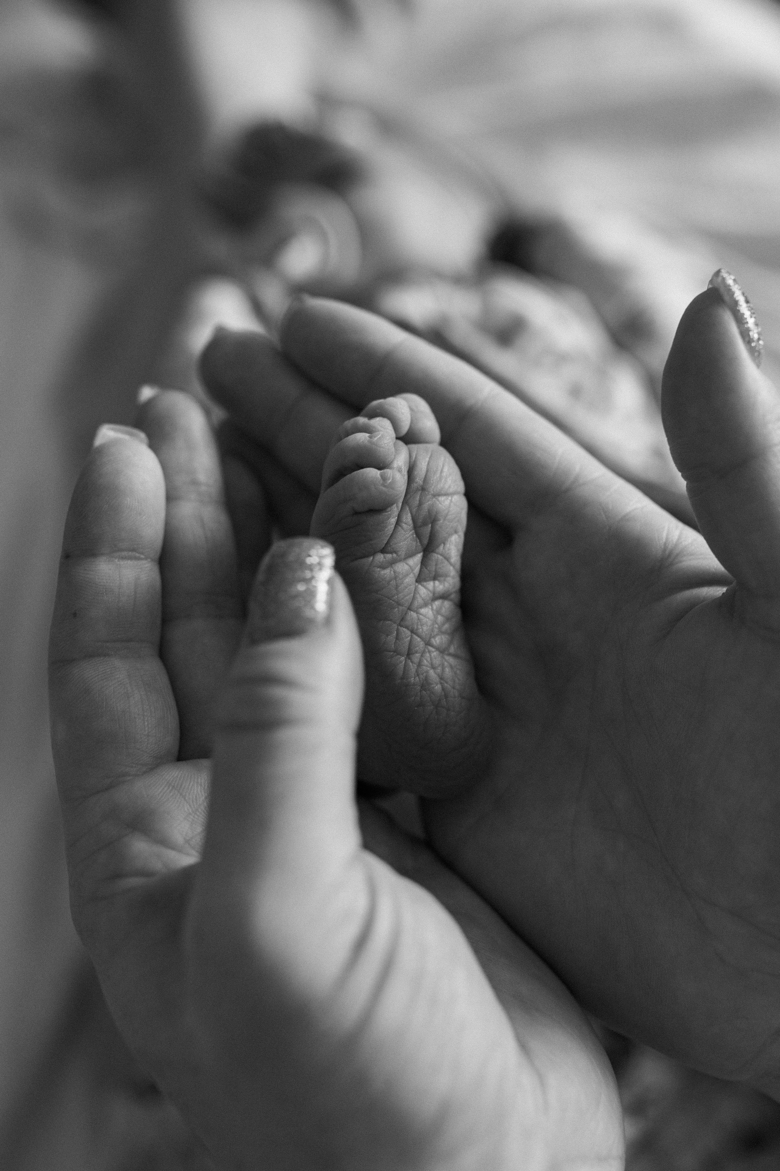 A tiny baby hand gently holds onto an adult finger in an intimate black and white close-up photograph.