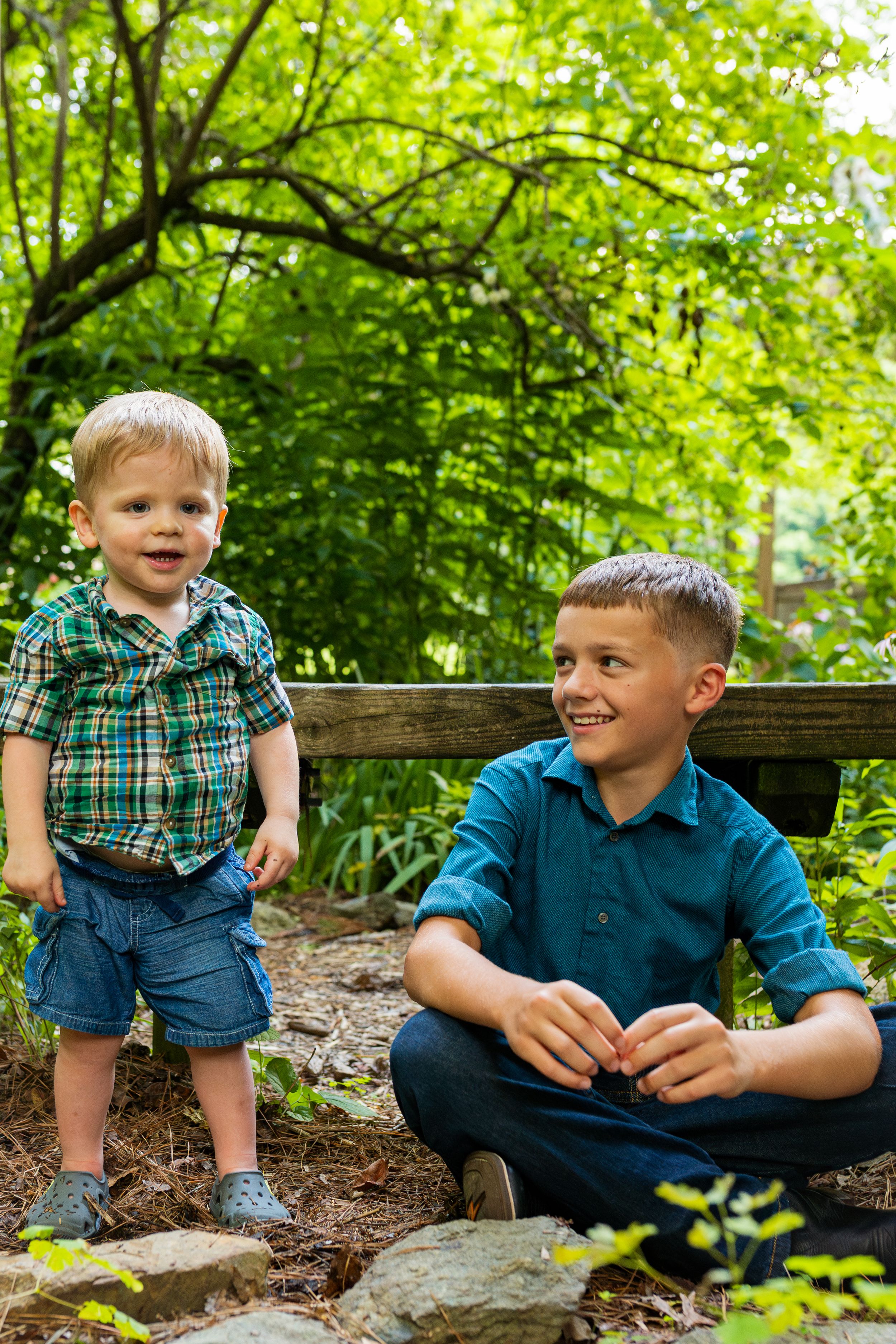 A young child sitting on natural stone steps surrounded by lush green foliage and trees in summer.