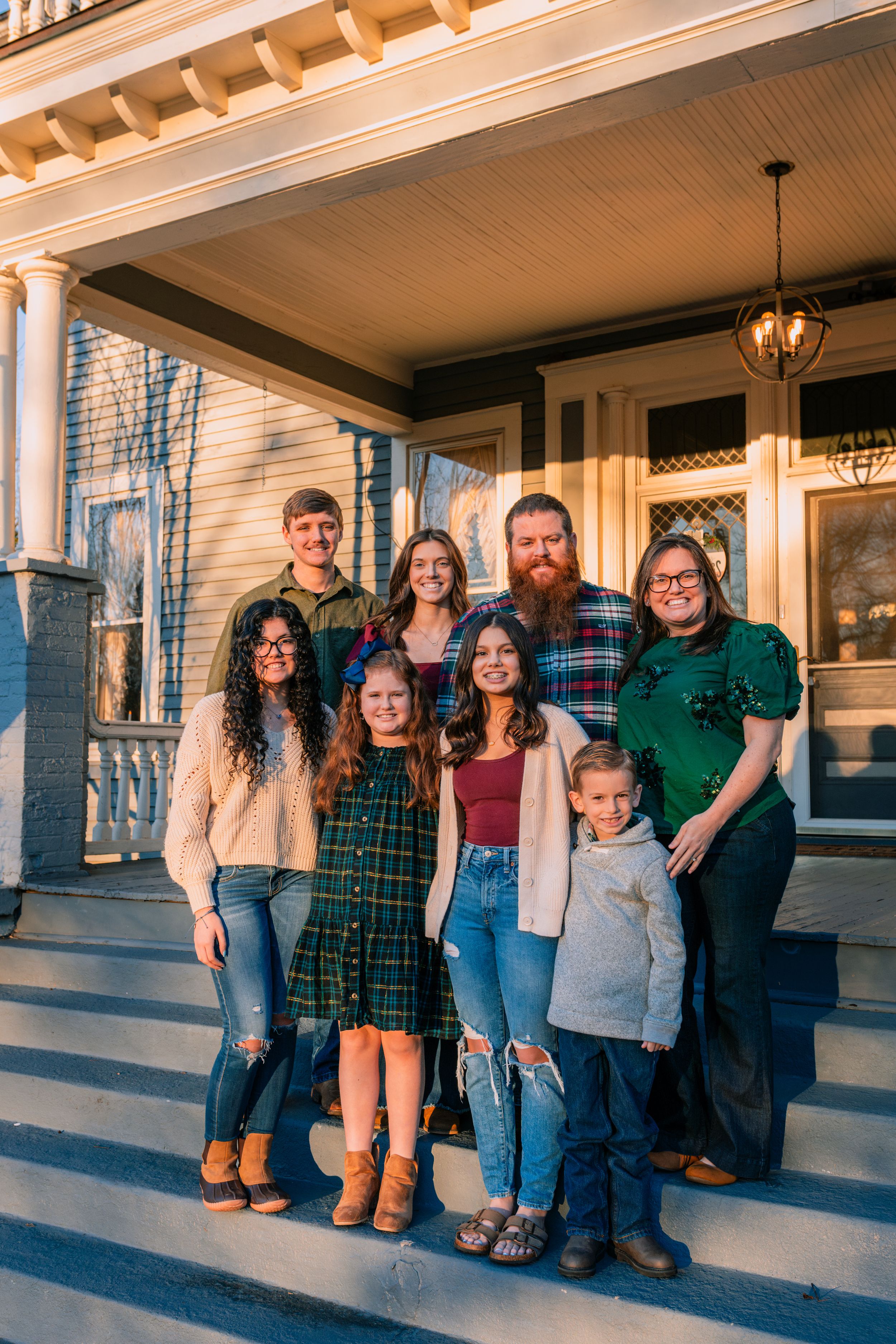 A group stands together on front porch steps of a historic home during a warm sunset.