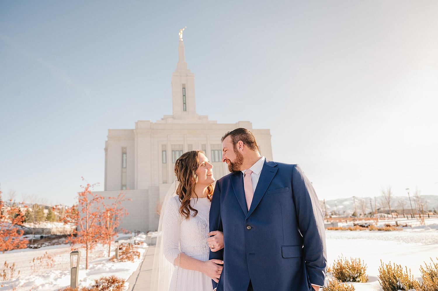 A wedding couple poses together against a majestic white temple building on a crisp winter day.