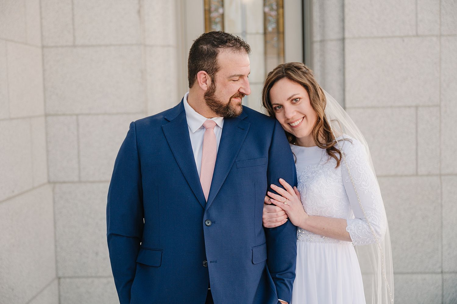 A happy couple shares an intimate moment outdoors by elegant white pillars for their engagement photos.