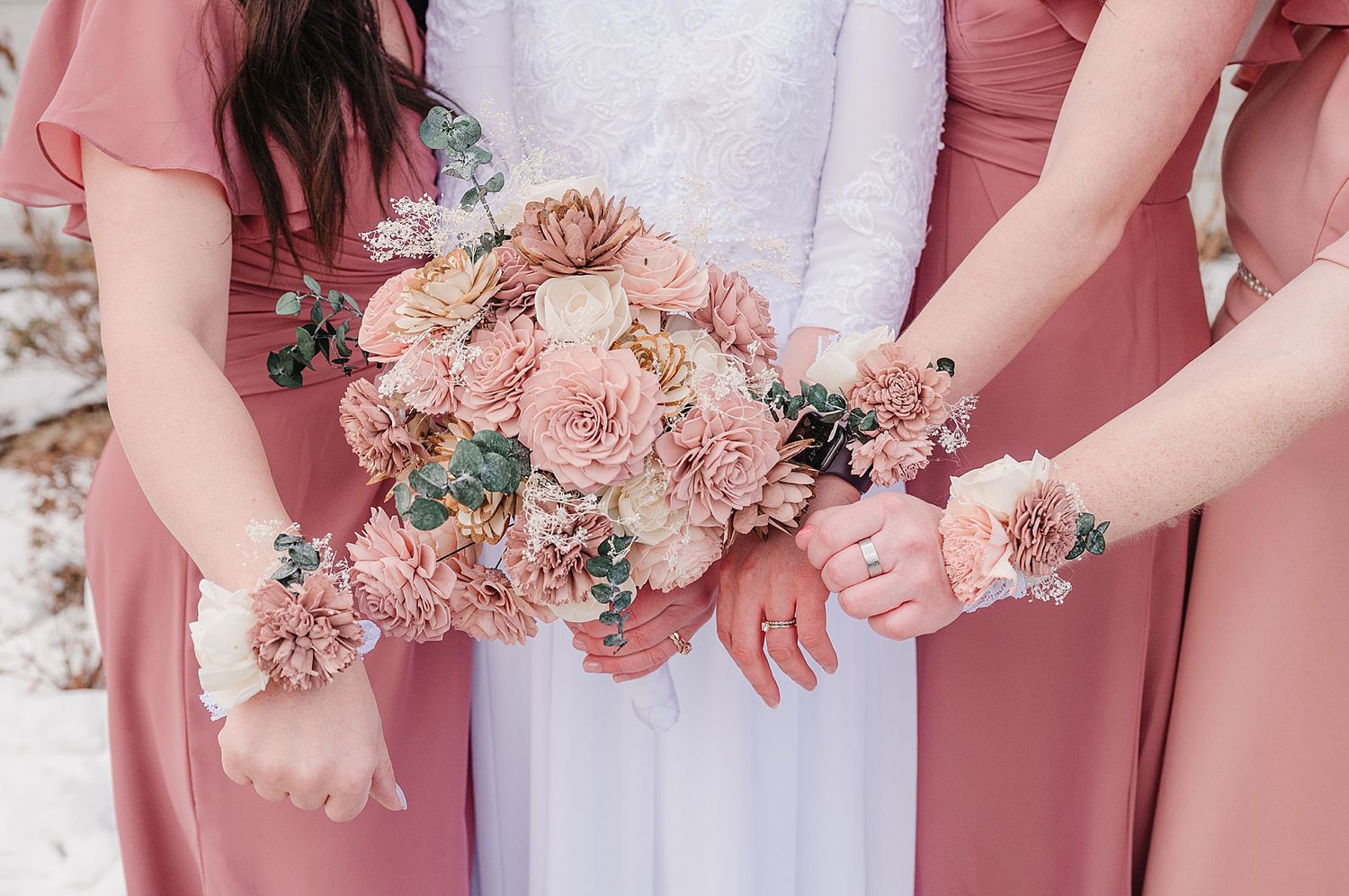 Close-up of bridesmaids wearing pink dresses showing matching corsages and wedding bouquet in blush tones.