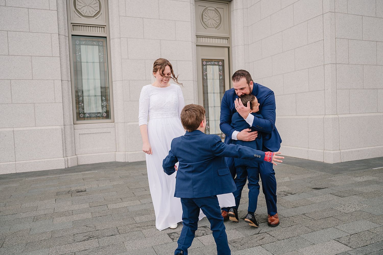 A joyful moment captured outside a white stone building with people in formal attire interacting on a paved terrace.