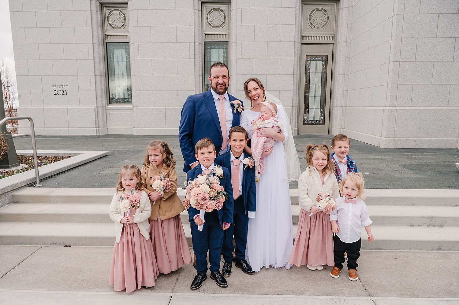 Family portrait on church steps wearing coordinated formal attire in white and dusty rose colors.