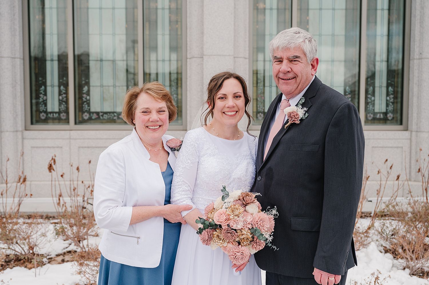 Happy couple on their wedding day posing with family outside a stone building in winter.