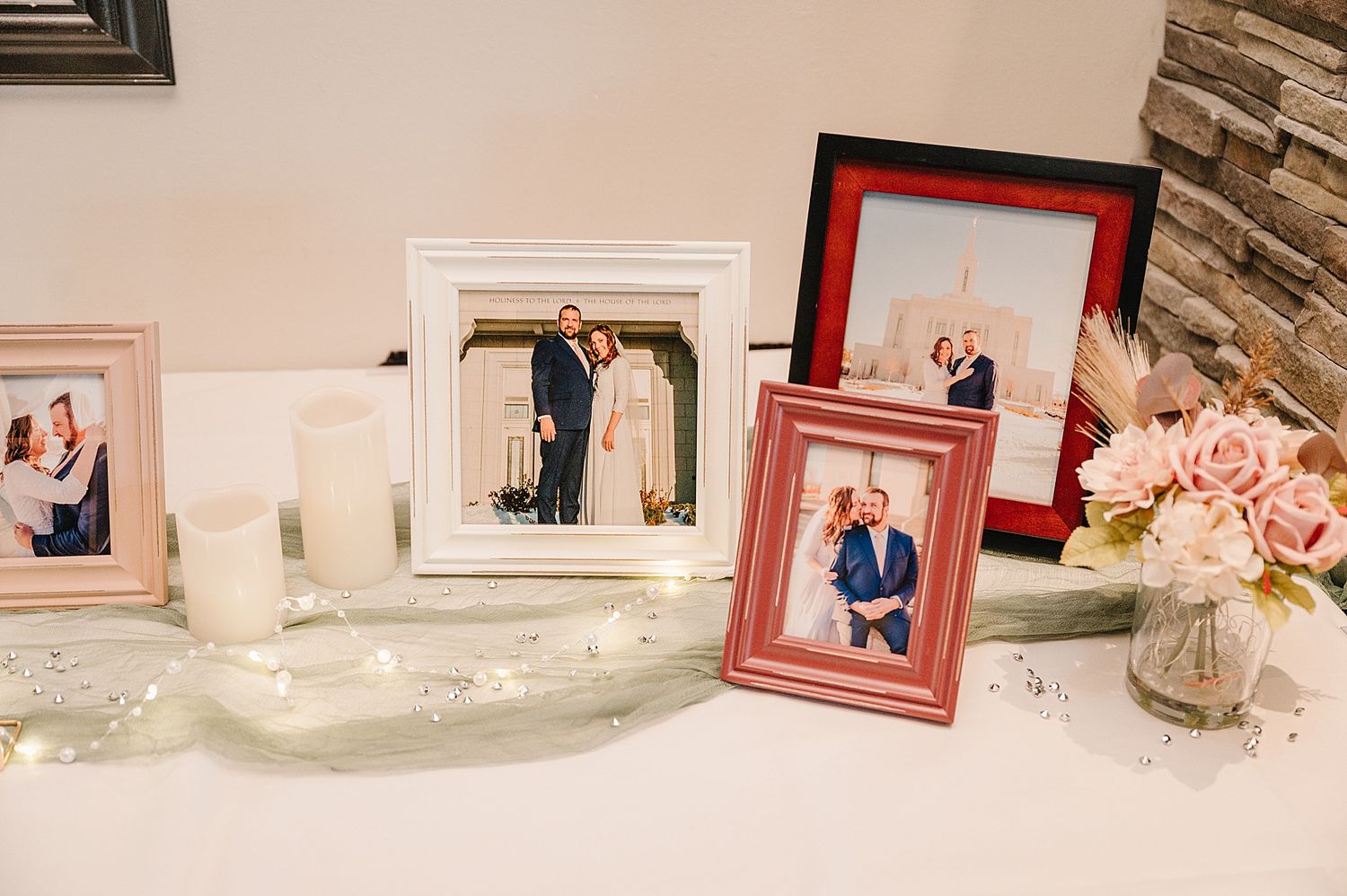 Decorated mantlepiece with framed photos, string lights, and pink roses in a glass vase.