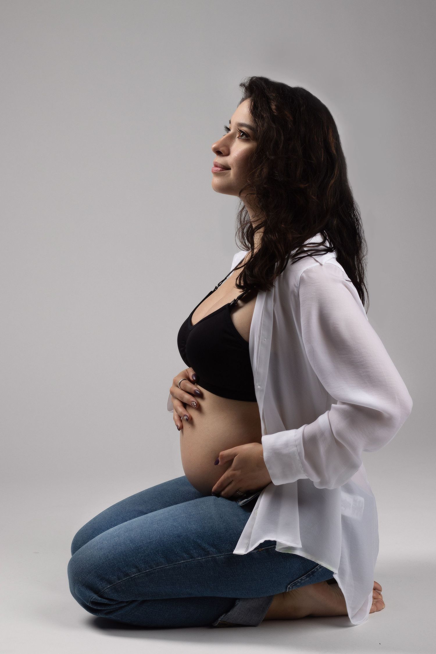 Serene maternity photoshoot sequence showing a woman in a white shirt and jeans posing against a grey background.