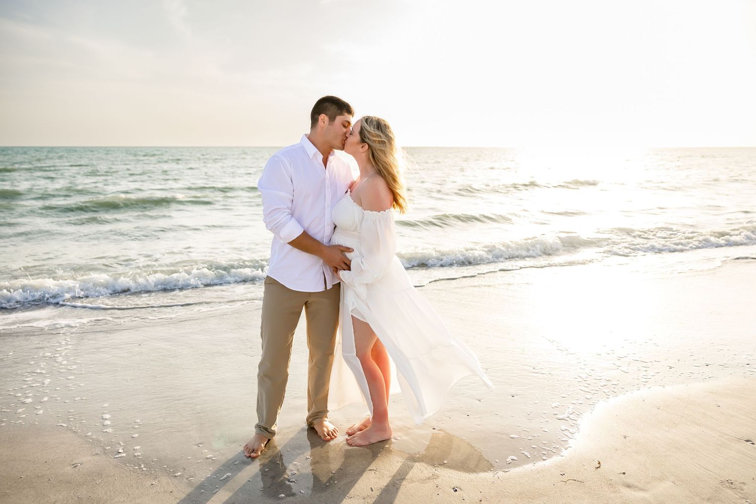 Romantic couple embracing and almost kissing on a sunny beach with ocean waves.