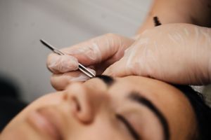 Close-up view of an eyebrow threading procedure being performed with white twisted cotton thread.