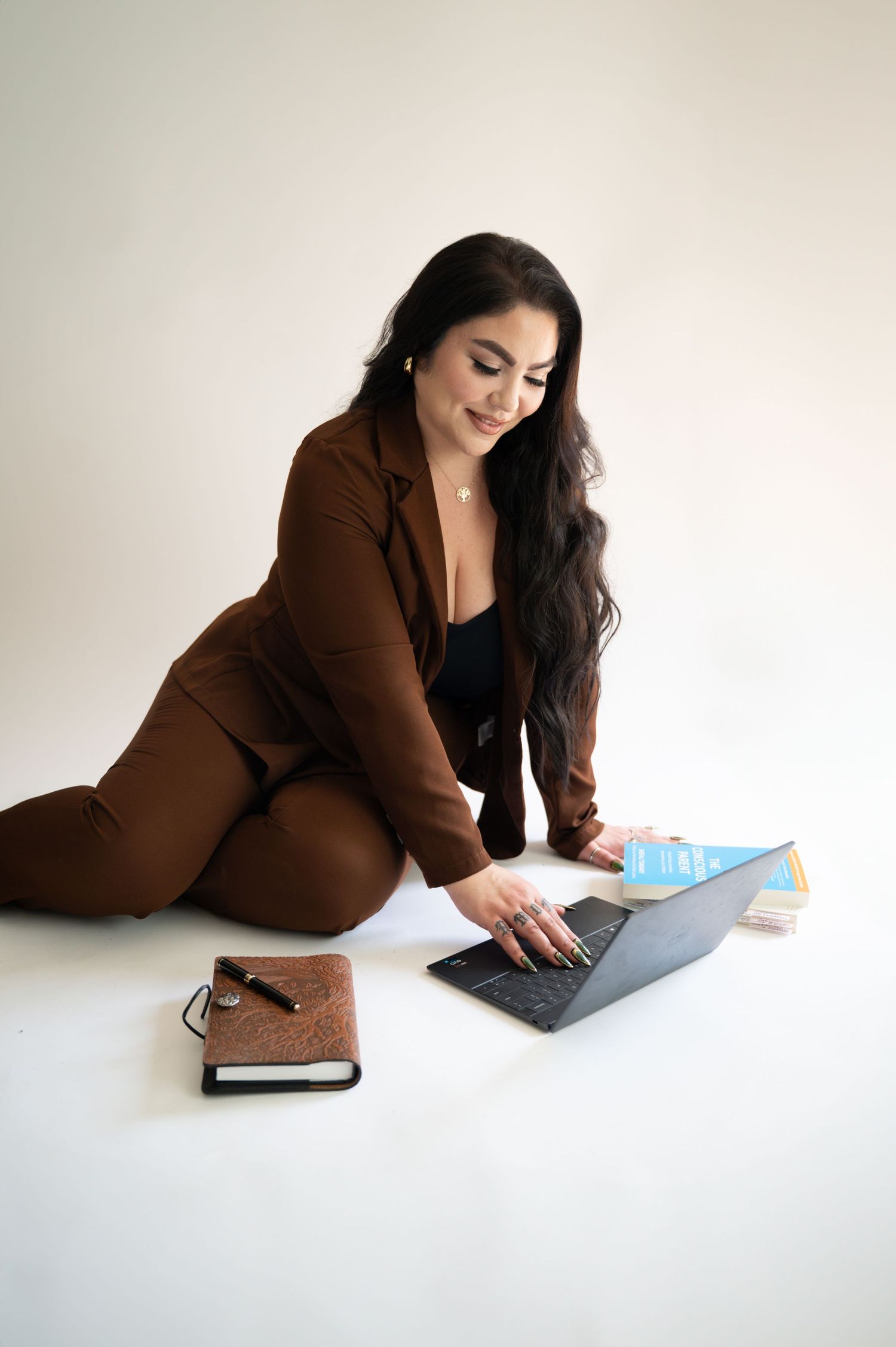 Professional working from home in brown suit using laptop computer with planner on white background floor setup.