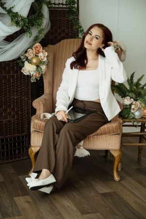 Modern fashion photo with brown wide-leg pants, white crop top and blazer in elegant setting with floral decor.