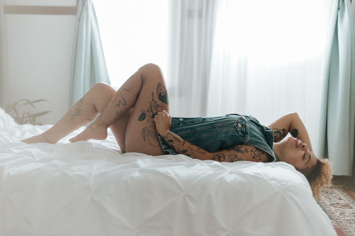 Relaxed lounging pose on white textured bedding with natural window light.