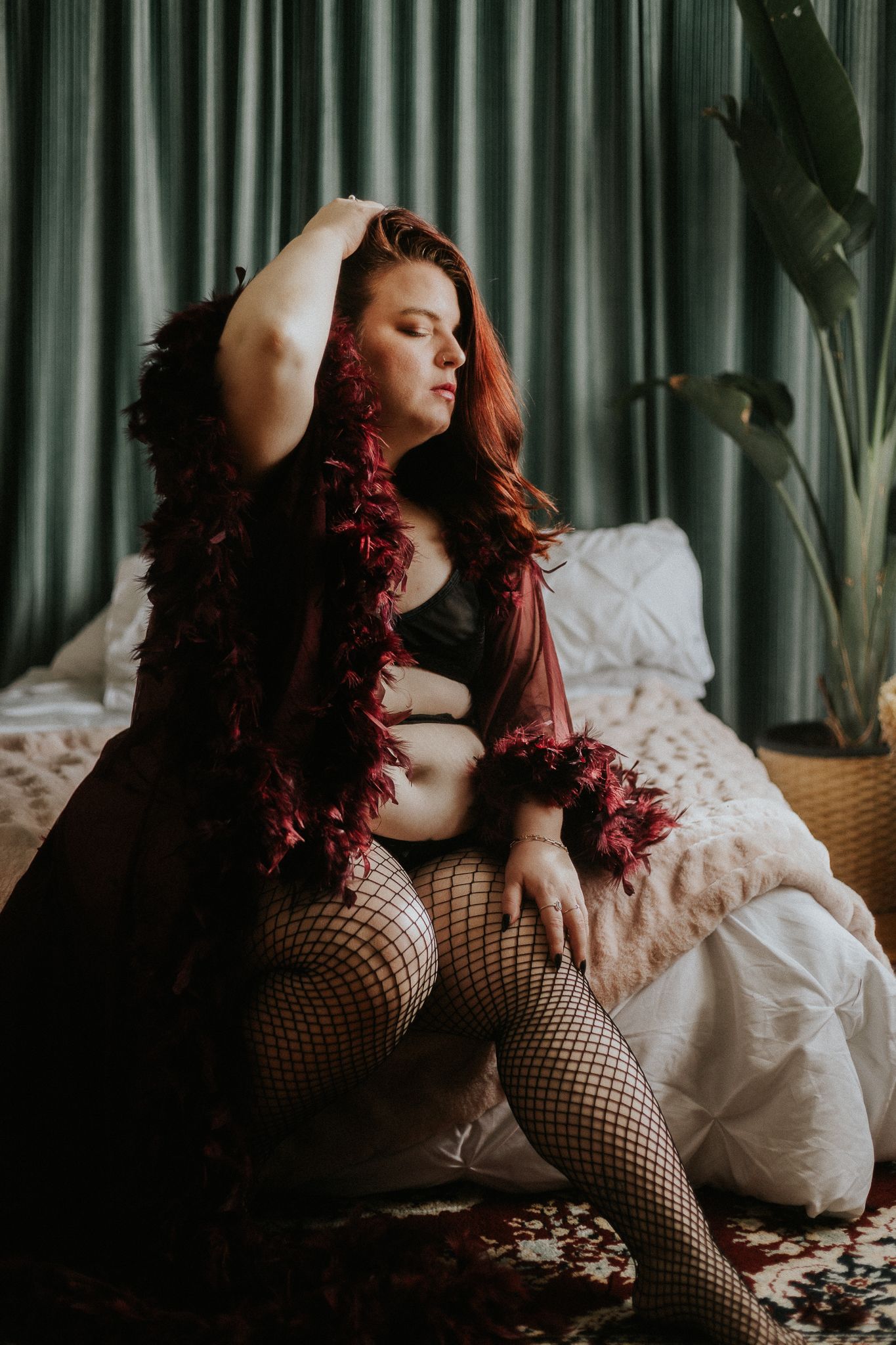 Artistic boudoir portrait with red feather boa against emerald curtains.