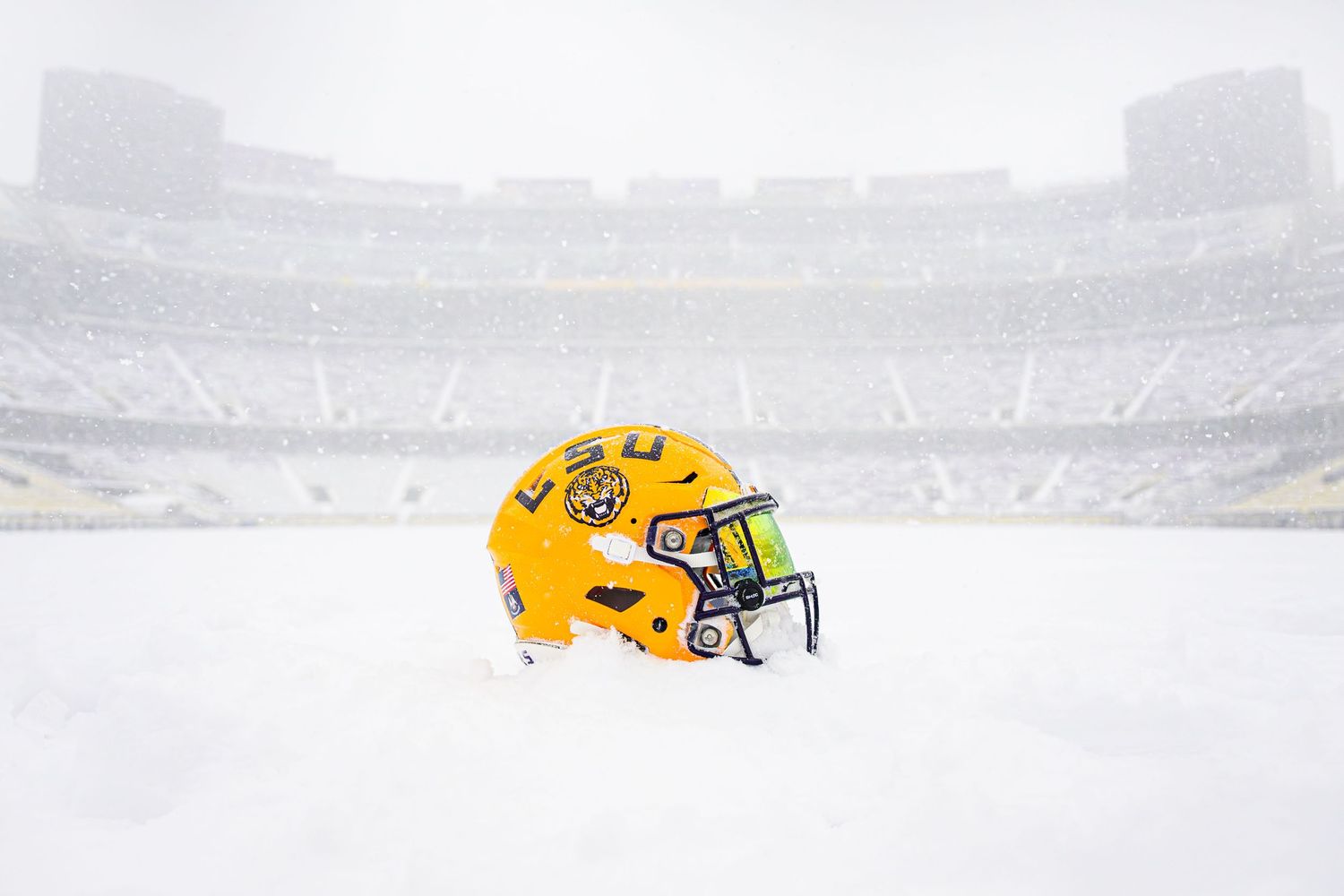 LSU football helmet sits alone on snowy field in empty stadium.