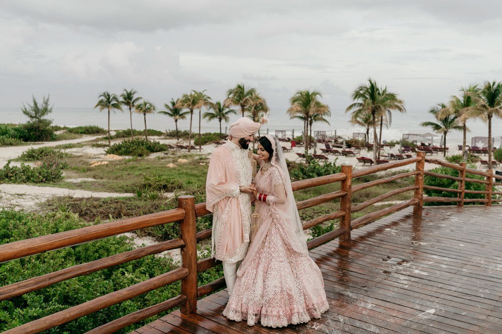A couple shares a romantic moment on a wooden boardwalk overlooking a tropical beach with palm trees on an overcast day.