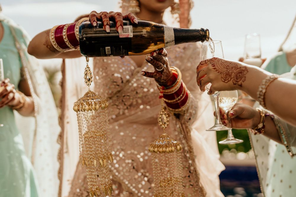Hands pouring wine during an Indian wedding celebration with traditional bangles and elegant attire visible.