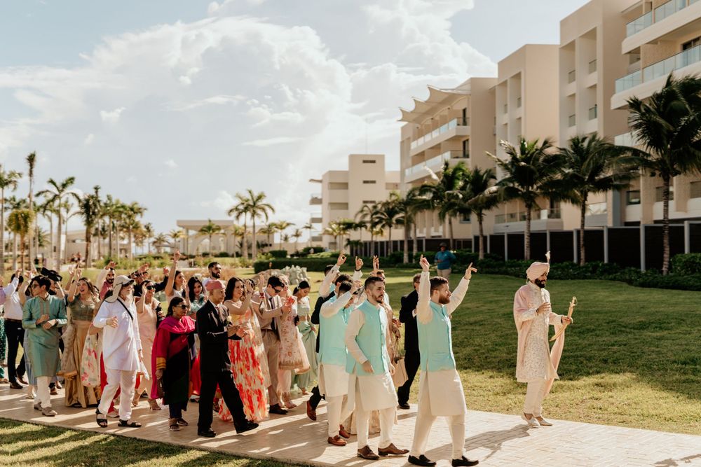 Wedding guests in colorful traditional Indian attire walking on grass with palm trees and resort buildings in background.