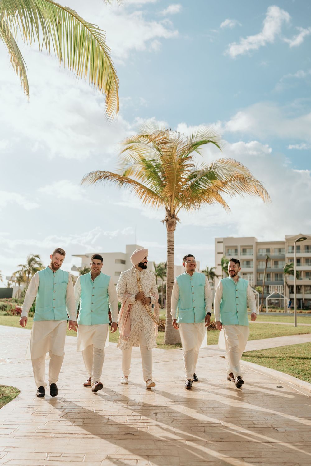 A group of men walking together in matching mint green shirts and white pants under palm trees at a tropical resort.