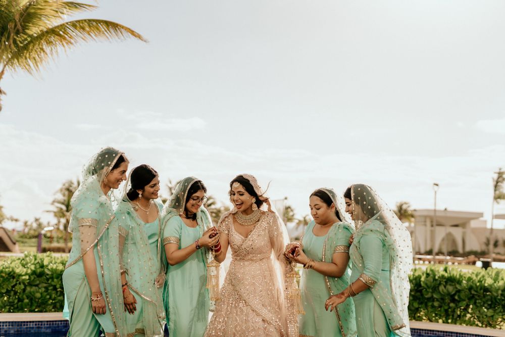 Bridesmaids wearing mint green dresses gather around a bride in a blush gown at a tropical beach resort.