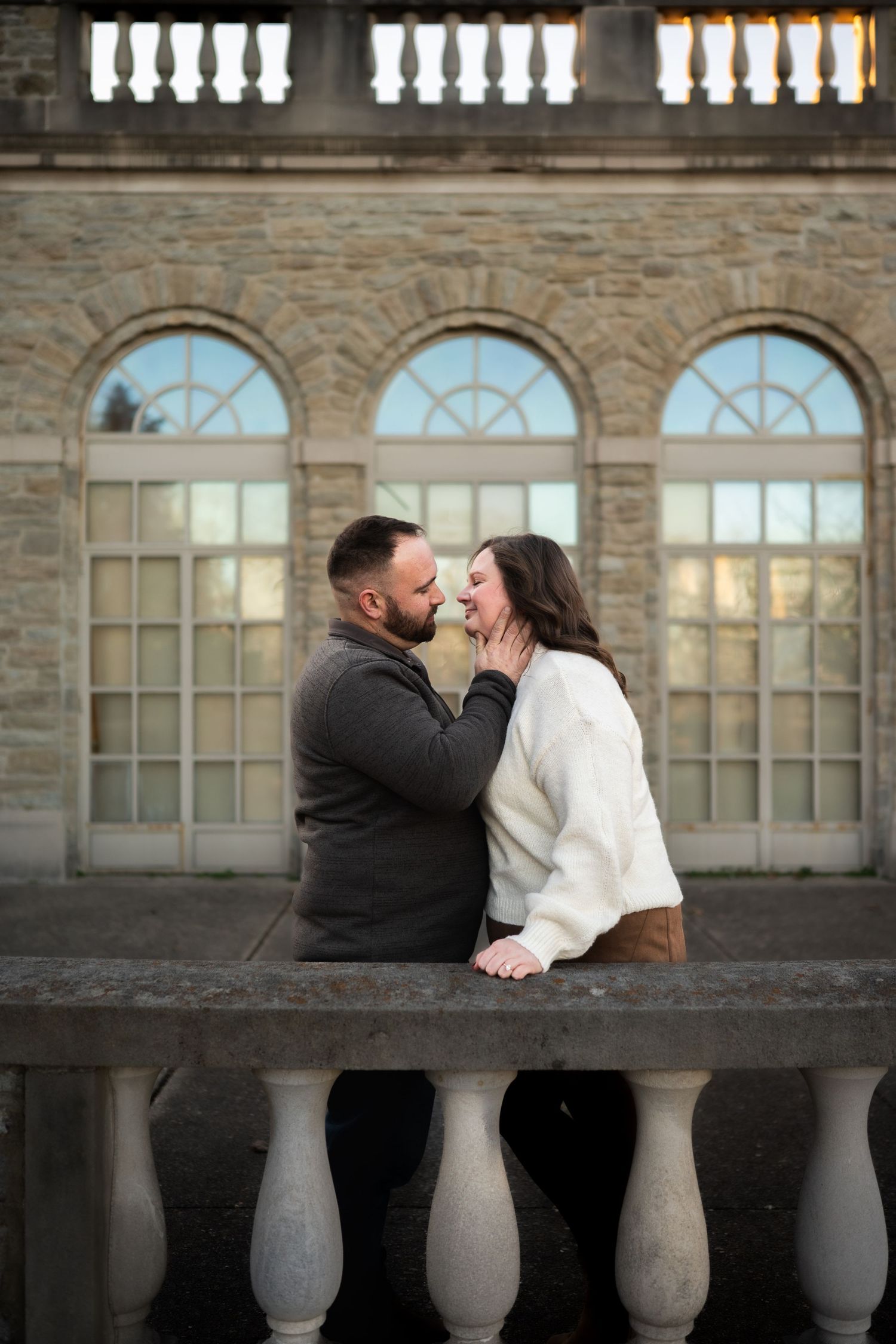 Couple sharing a romantic moment while sitting on a stone ledge with arched windows in the background.