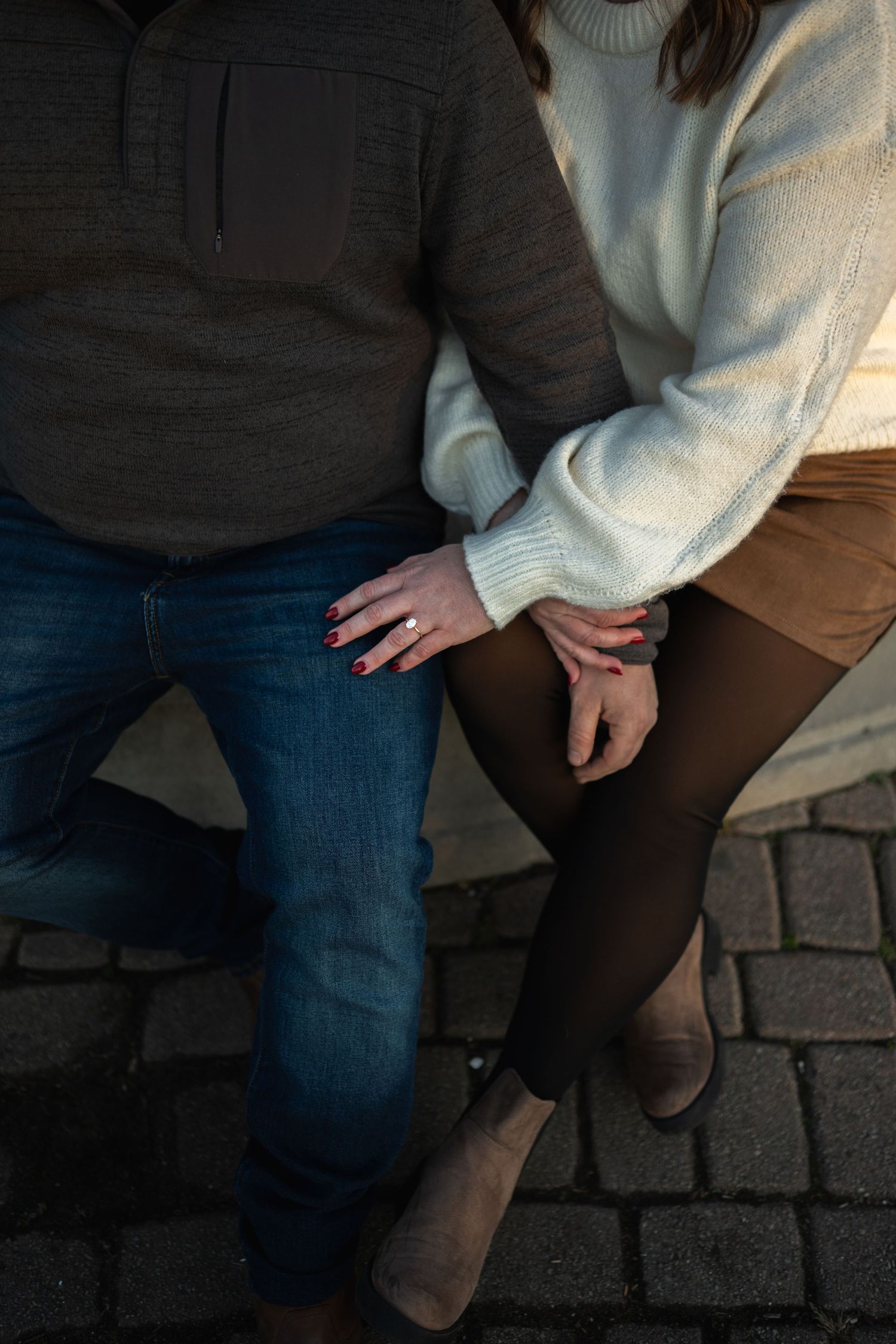 Two people in casual clothing stand close together on a brick paved surface showing only their lower bodies.